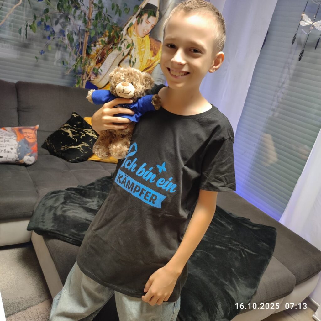 make-a-wish-oesterreich_erfuellte-wuensche_Fabian (12) Fabian hält einen Make-A-Wish-Teddybären und trägt ein Shirt mit der Aufschrift „Ich bin ein Kämpfer“ zu Hause.