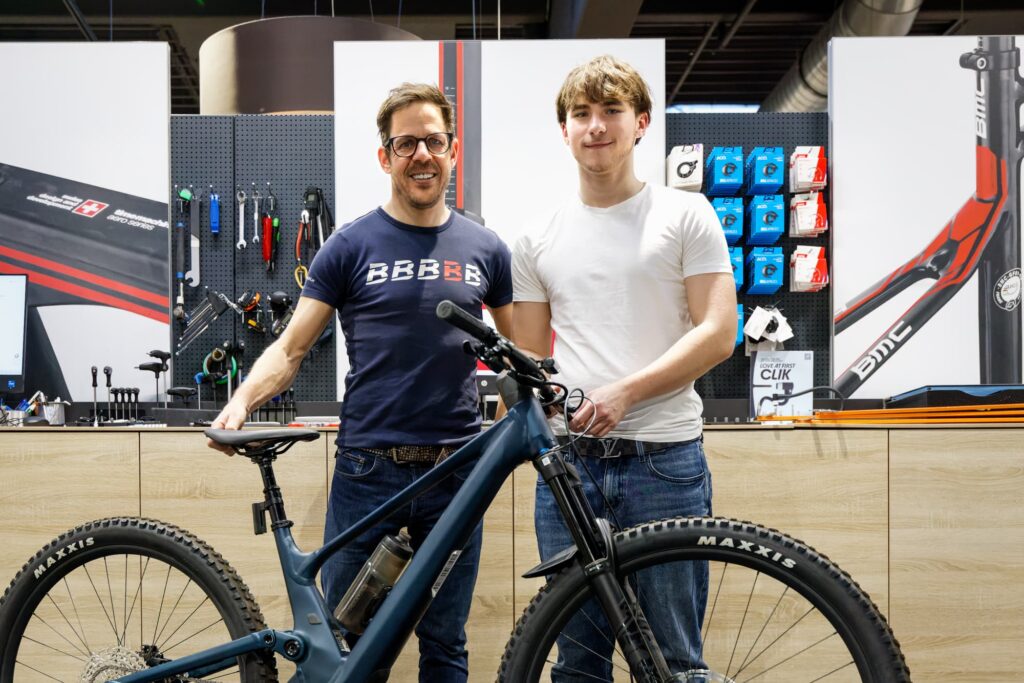 make-a-wish-oesterreich_erfuellte-wuensche_Daniel (3) Spender Bernhard Kohl und Wunschkind Daniel stehen lächelnd hinter dem dunkelblauen Mountainbike